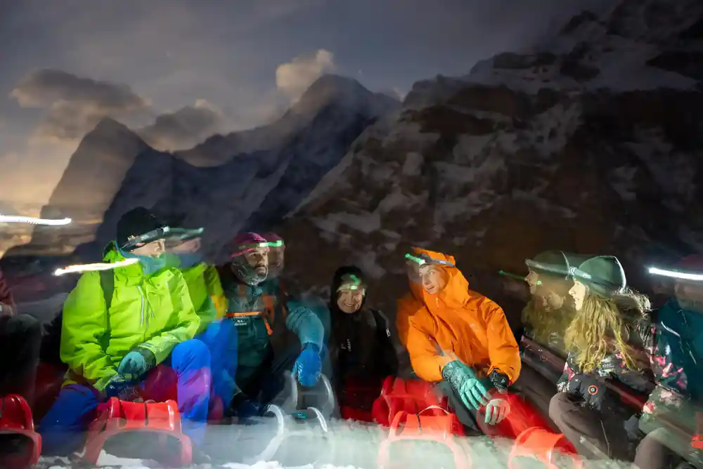 Four sledders in coloured jackets and headlamps waiting on the snow