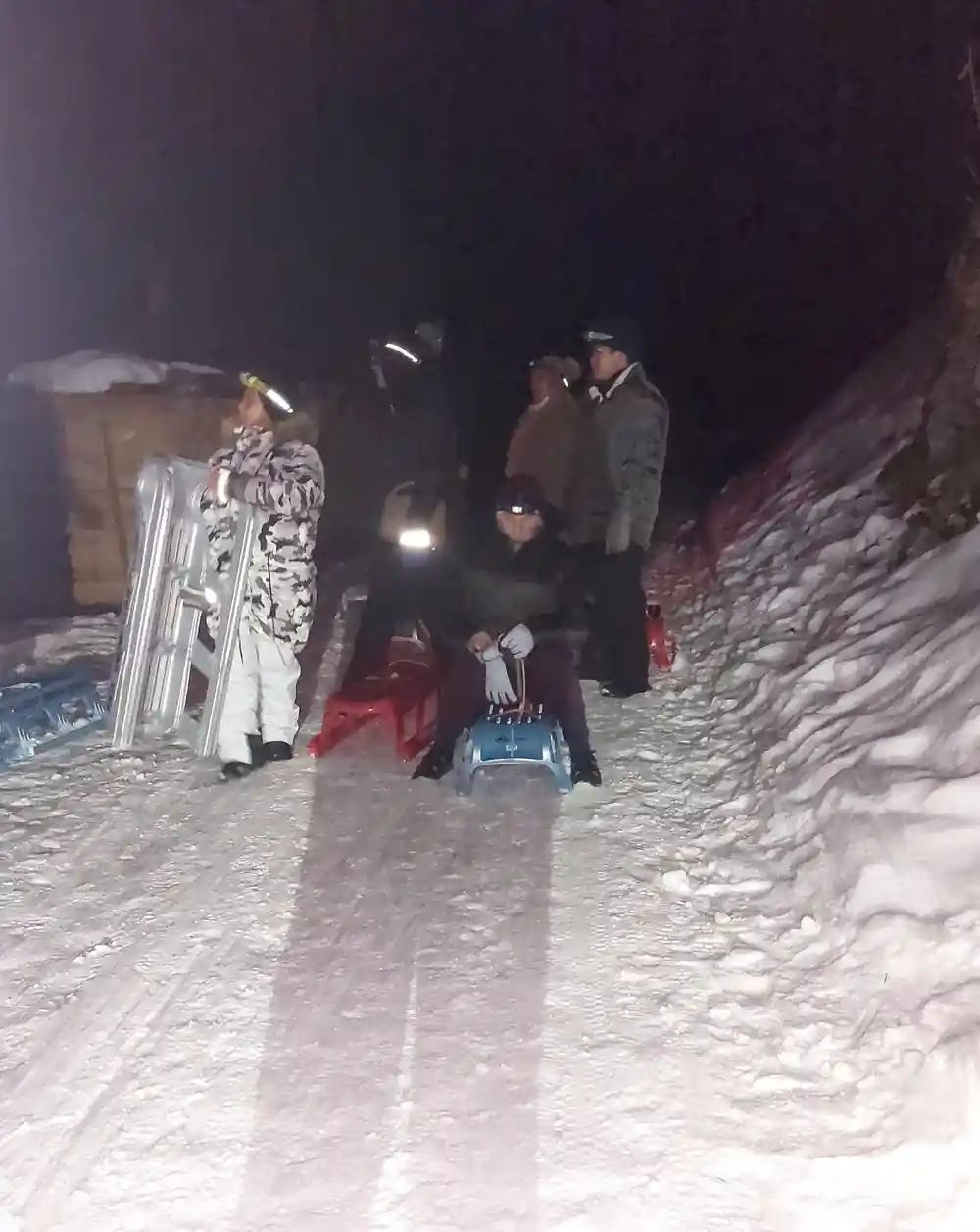 A group gathering with sleds at a lit meeting point in the snow