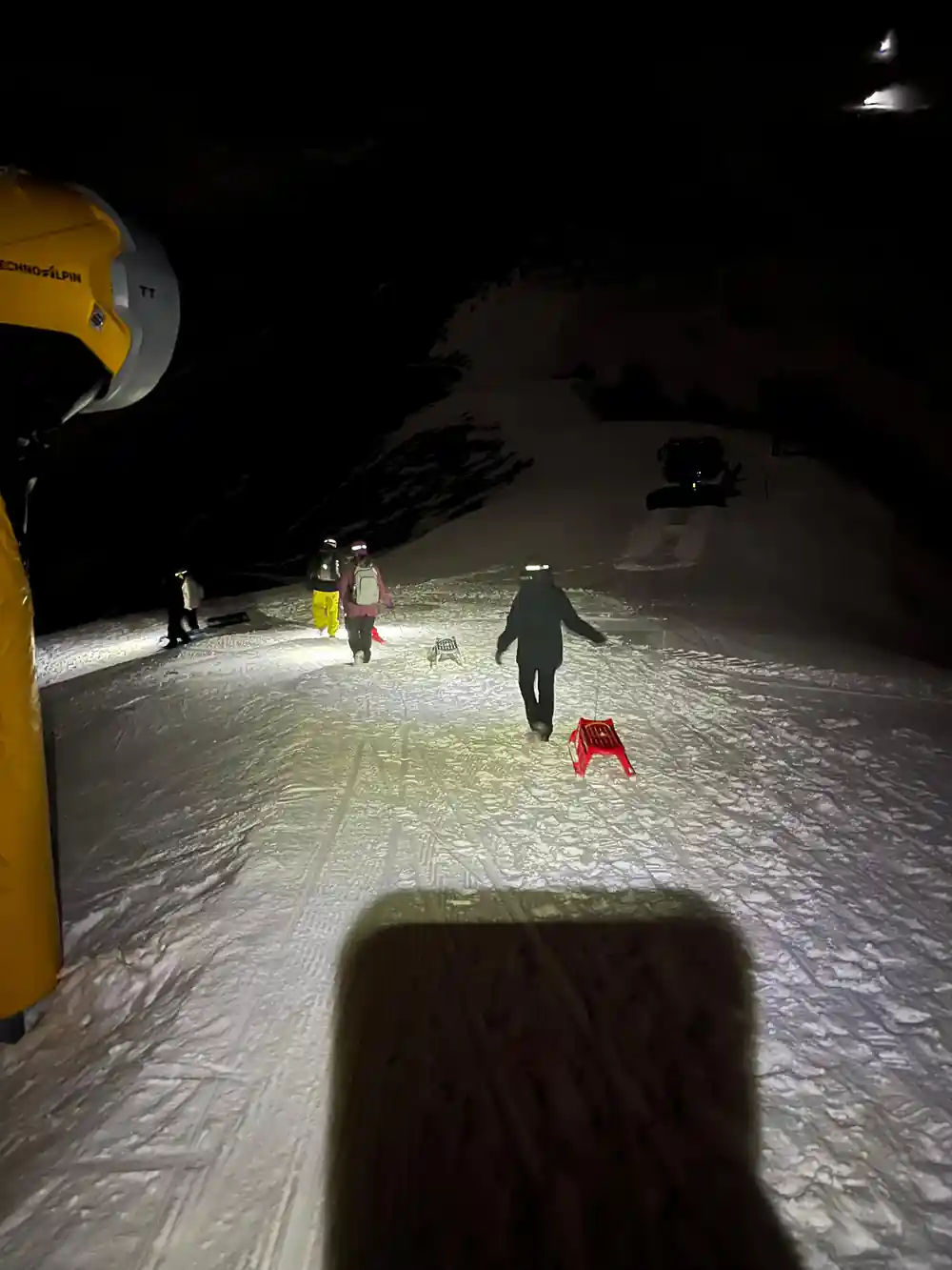 A headlamp beam thrown down the track, figures ahead and a red sled