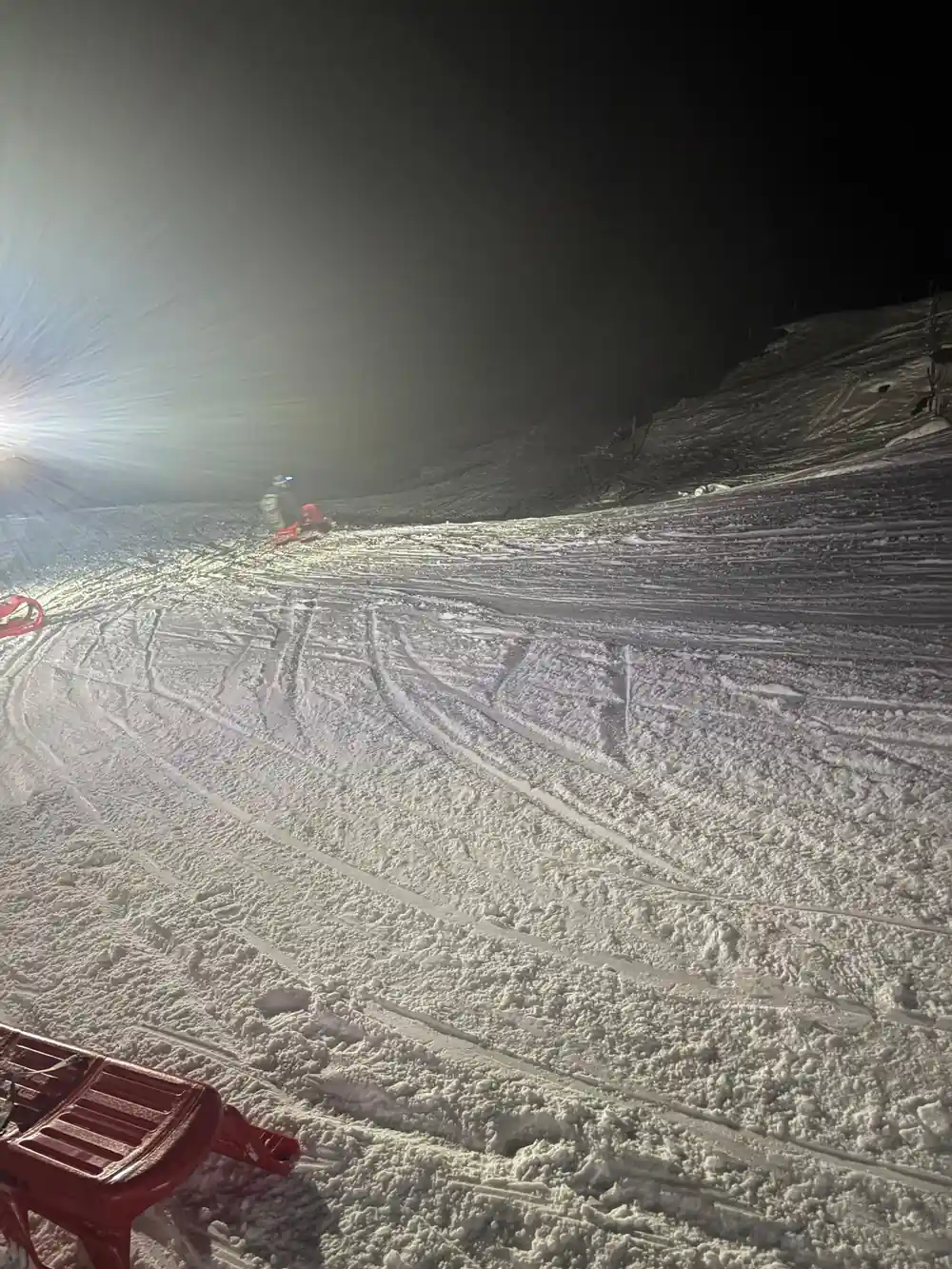A lit groomed track curving away with a distant sledder on it