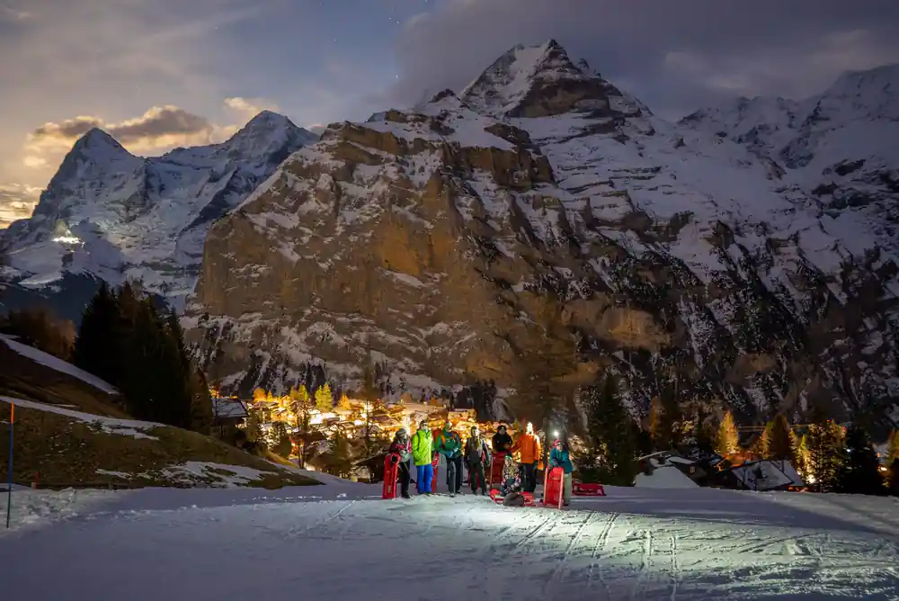 The massif at dusk above a valley of village lights, a group on the snow below