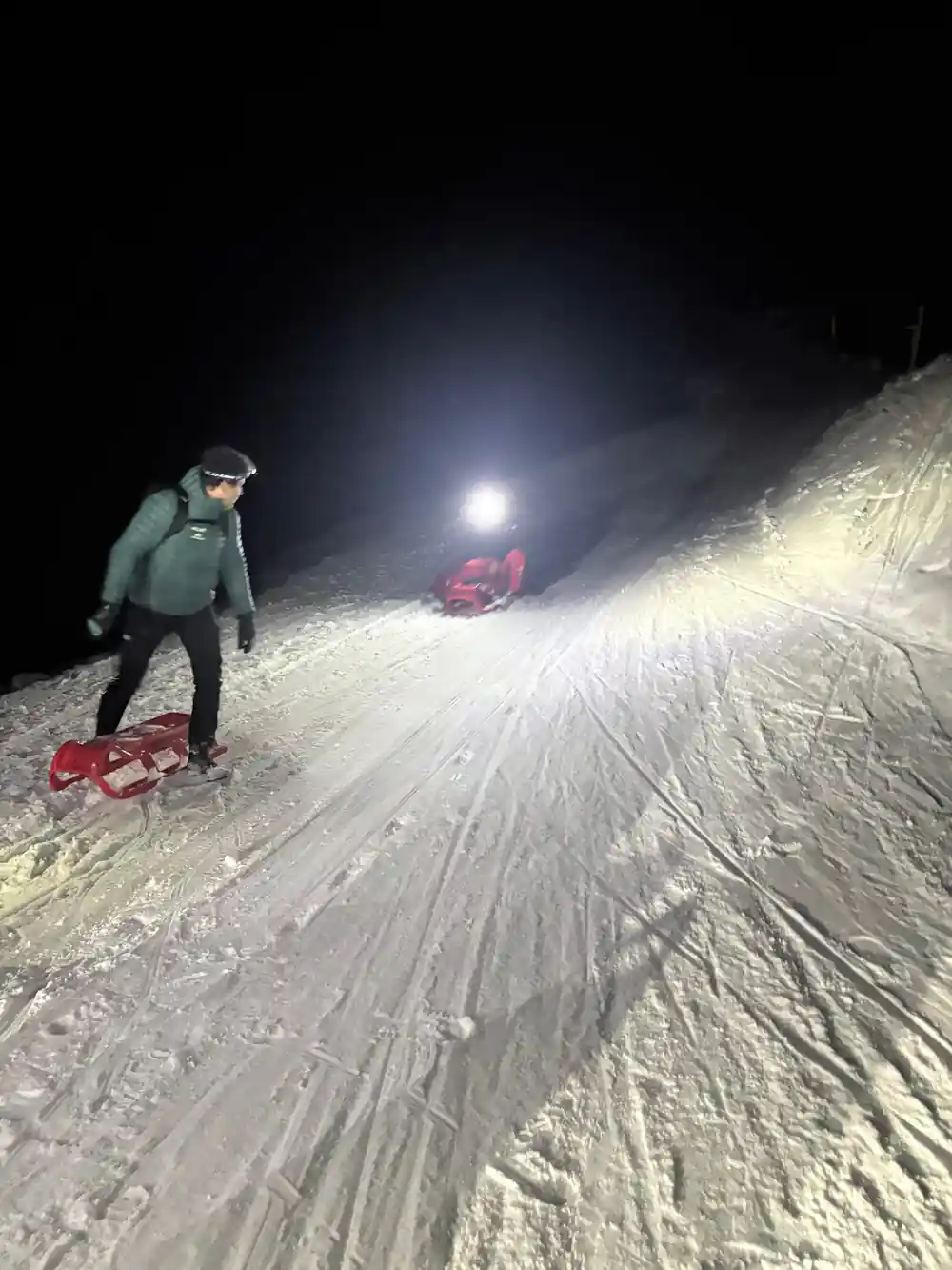 A person walking up a lit track pulling a red sled behind them