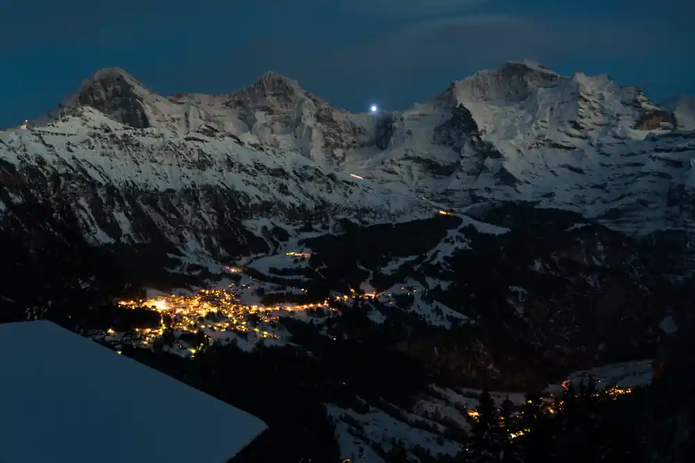 Snowy peaks standing over a valley full of village lights at night