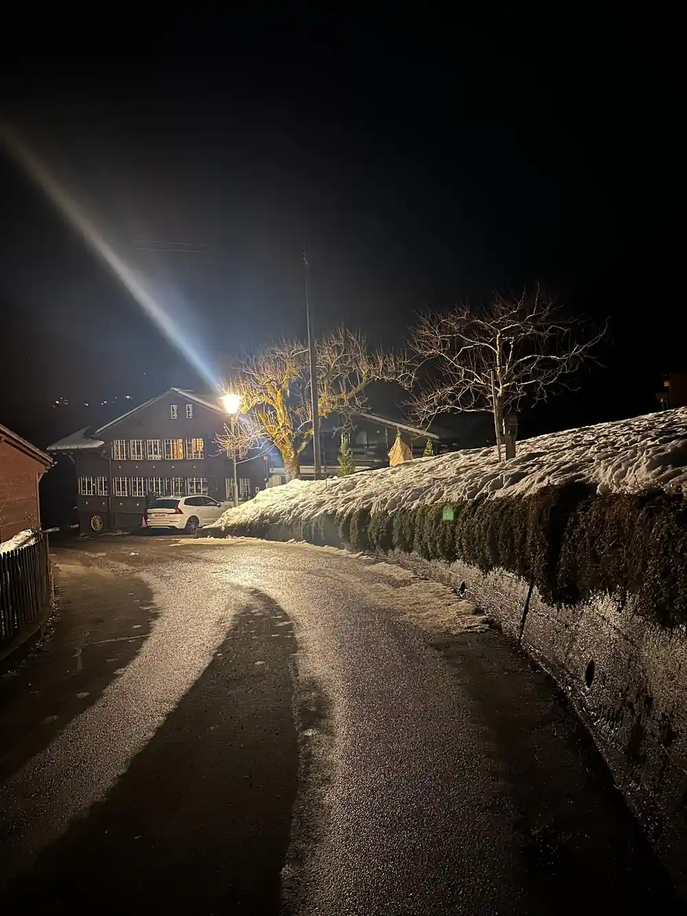 A village street at night, a lit chalet and banked snow along the road